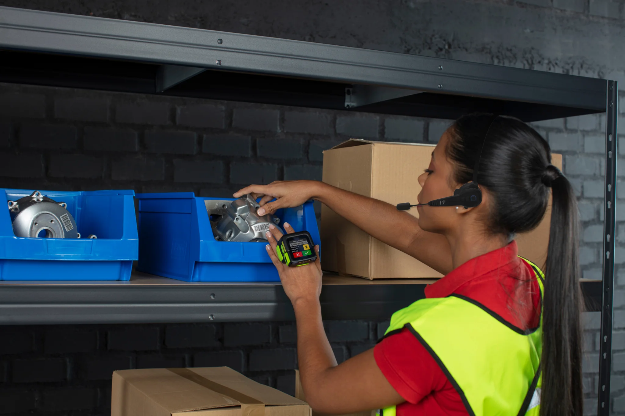 A warehouse operator, equipped with a headset and a wearable hand device is picking the items from a shelf.